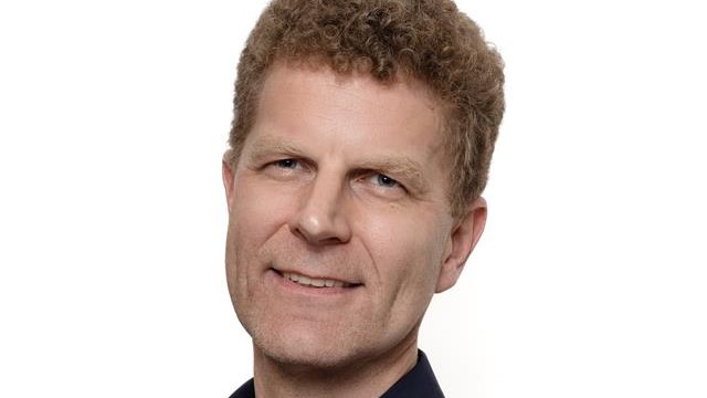 Porträtfoto von Gerald Beuchelt, er lächelt in die Kamera. Der Hintergrund ist neutral weiss.