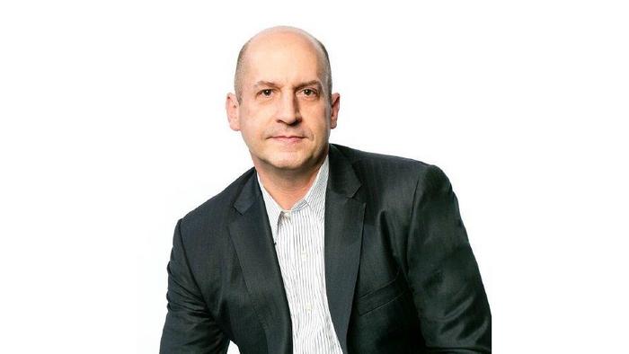 Das Bild zeigt einen mittelalten Herrn ohne Kopfhaar. Er trägt einen dunklen Anzug. 