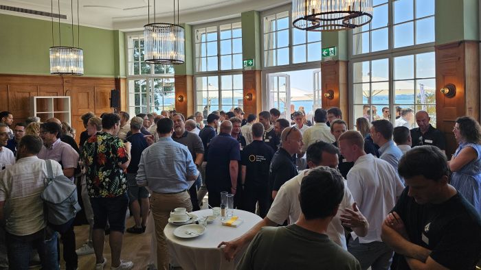 Auf dem Bild sind viele Personen im Theater Casino Zug zu sehen beim Apéro und Networking. Hinter ihnen ist der Zugersee zu sehen.